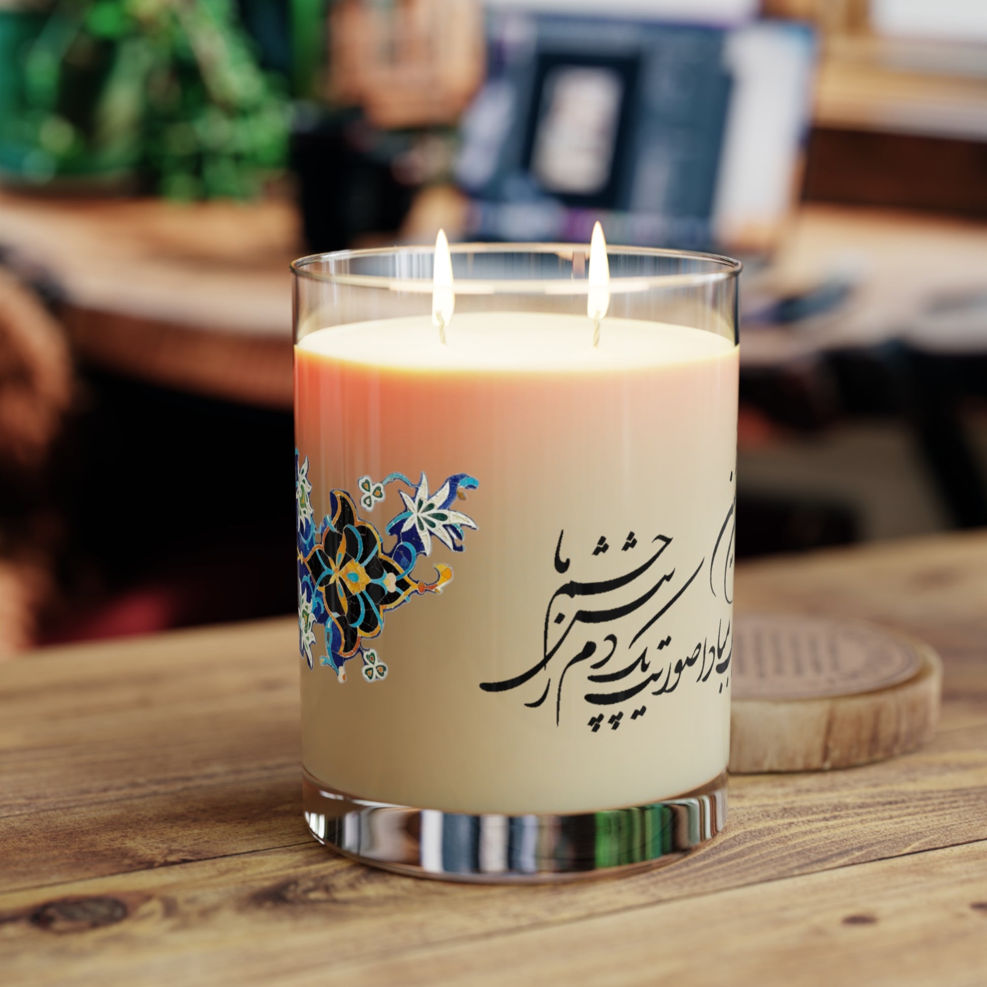 Candle with decorative label featuring Farsi calligraphy and floral designs on a white background