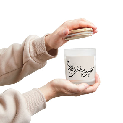 Person holding a white candle with Farsi calligraphy text and a wooden lid.