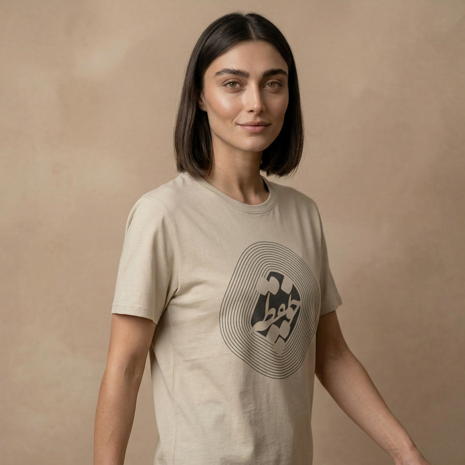 Woman wearing a beige t-shirt with a graphic design and farsi calligraphy on a beige background