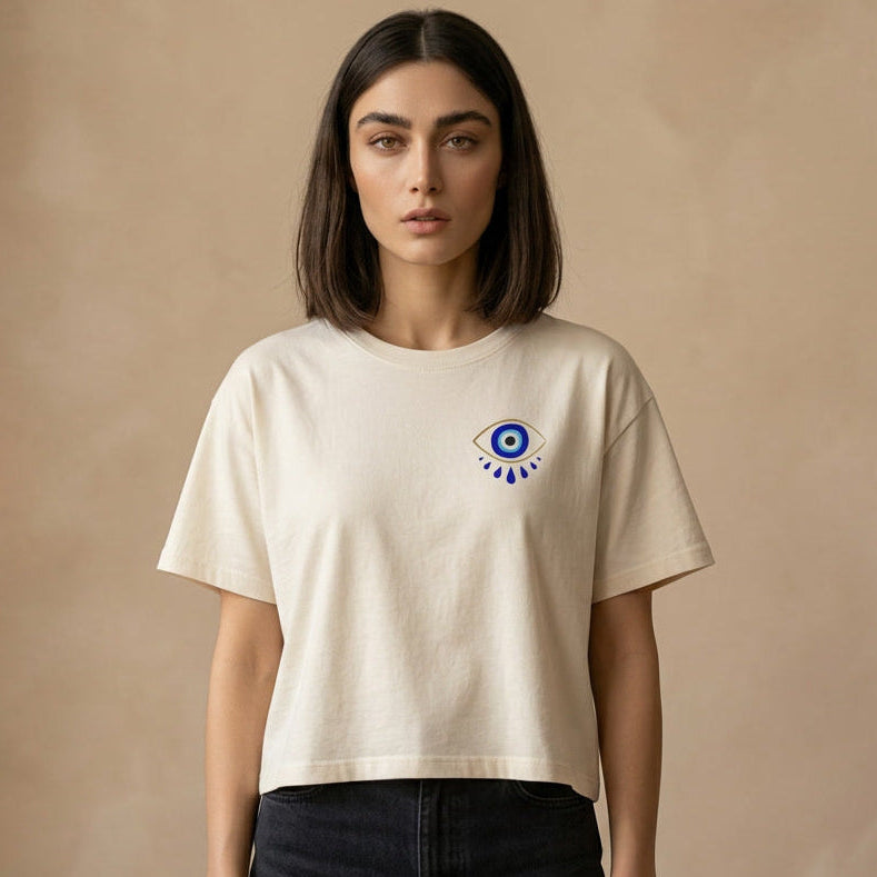 Woman wearing a beige t-shirt with an evil eye graphic on the chest and a beige background